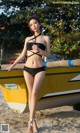 A woman in a black bikini standing next to a yellow boat.