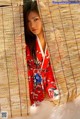 A woman in a red kimono is peeking out from behind a bamboo curtain.