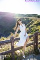 A woman in a white dress leaning on a wooden fence.