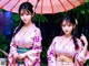 Two young women in kimonos standing under an umbrella.