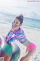 A woman in a pink bikini sitting on an exercise ball on the beach.