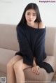 A woman sitting on a couch wearing a black sweater.