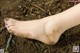 A woman's foot covered in dirt on the ground.