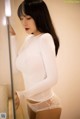 A woman in a white bodysuit leaning against a mirror.