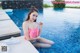 A woman in a pink bikini sitting by a swimming pool.