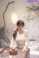 A woman in a white dress sitting at a table with a teapot.