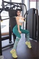 A woman in a white top and green leggings sitting on a gym machine.