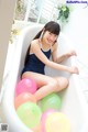 A woman sitting in a bathtub filled with colorful balloons.