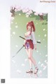 A woman with red hair in a ponytail, wearing a white top and purple shorts, holding a sword, standing under cherry blossoms.