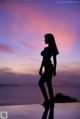 A silhouette of a woman standing on the edge of a swimming pool.