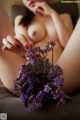 A naked woman sitting on a couch holding a bunch of purple flowers.