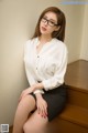 A woman in a white shirt and black skirt sitting on some stairs.