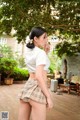 A woman in a white shirt and plaid skirt smoking a cigarette.