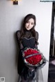 A woman in a black dress holding a bouquet of red roses.