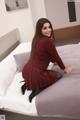 A woman in a red dress sitting on a bed.