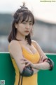 A woman in a yellow tank top leaning against a green wall.