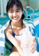 A young woman sitting by a swimming pool holding a bottle of water.