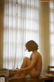 A naked woman sitting on a table in front of a window.