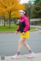 A woman in a pink jacket and yellow skirt is walking down the street.