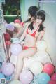 A woman in a red bikini sitting on a bed surrounded by balloons.