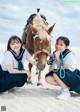 Two girls in school uniforms pose with a horse on the beach.