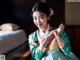 A woman in a green and pink hanbok sitting on a bed.