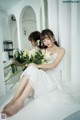 A woman in a white dress sitting on a window sill holding a bouquet of flowers.