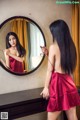 A woman in a red dress looking at herself in the mirror.