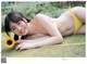 A woman in a yellow bikini laying on the grass.