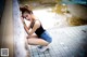 A woman in a black tank top and denim shorts leaning against a wall.