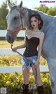 A woman standing next to a white horse in a field.