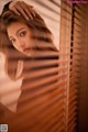 A woman leaning against a window with blinds.