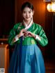 A woman in a green and blue hanbok poses for a picture.