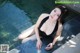 A woman in a black bathing suit sitting by a pool.