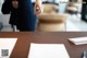 A woman standing at a table with papers and a pen.